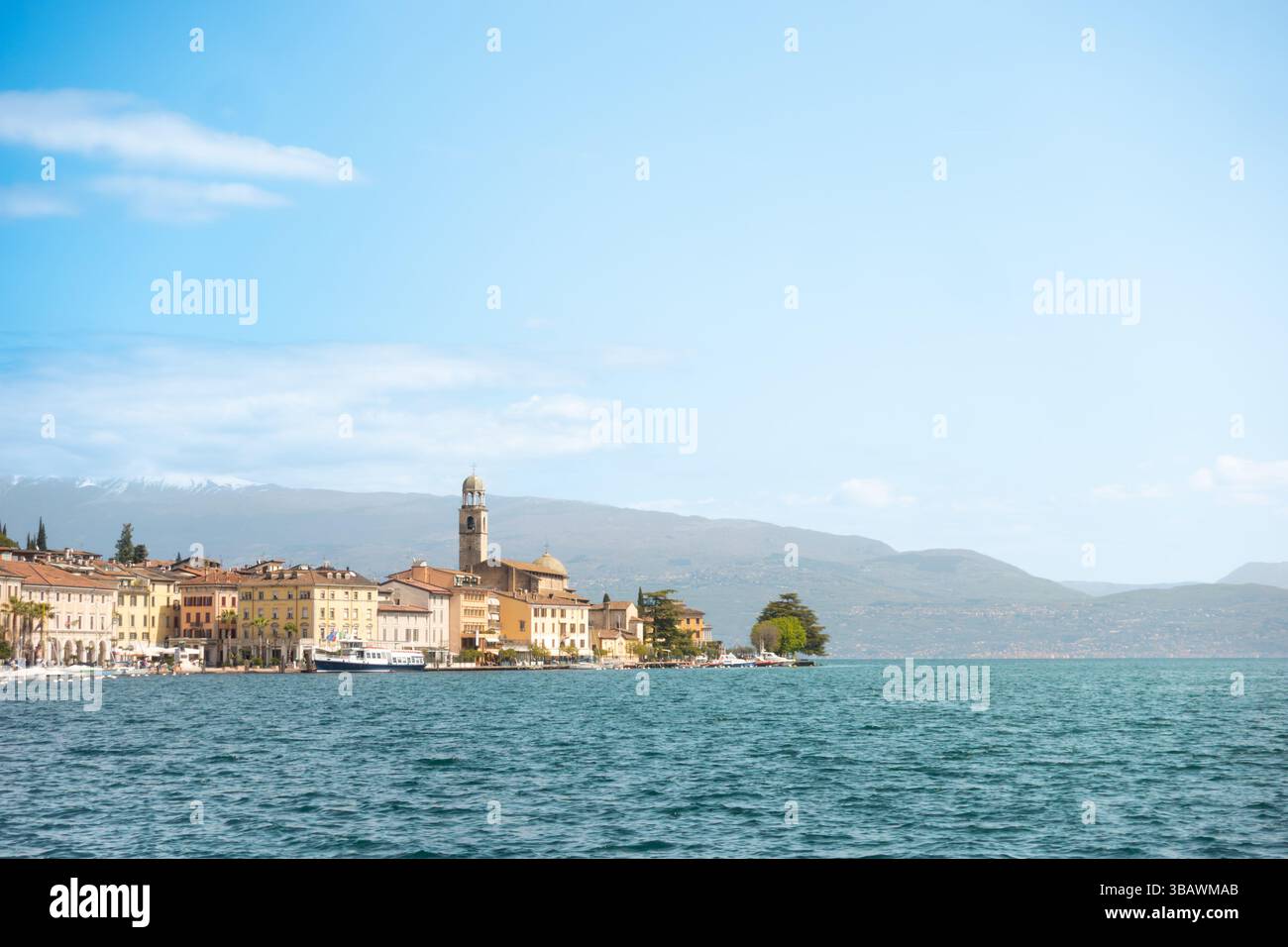 Vue panoramique de la ville côtière de Salò par le lac Lago di Garda avec tour d'église emblématique en face des montagnes des alpes en arrière-plan par temps clair Banque D'Images