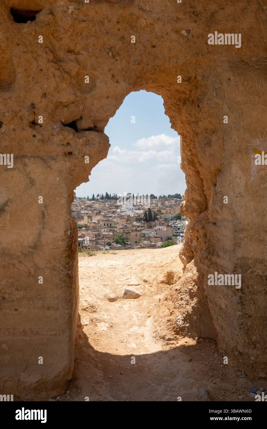 À travers une brèche dans les anciens murs de Fès, une vue sur les maisons traditionnelles marocaines émerge, révélant un mélange d’histoire et d’architecture encadrée par les mauvaises herbes Banque D'Images