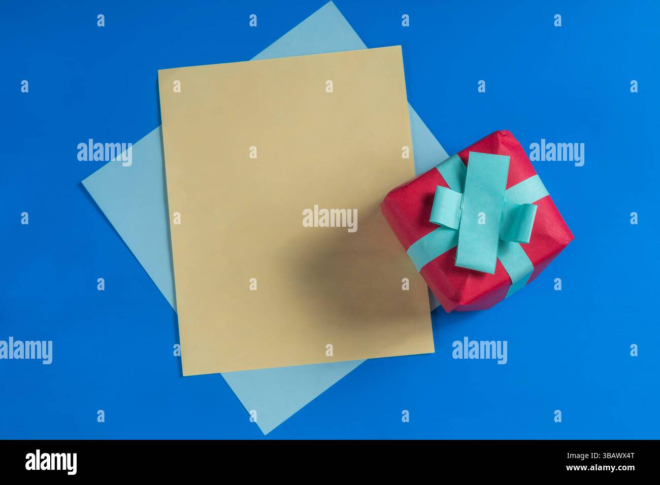Une boîte cadeau rouge enveloppée dans un ruban bleu sur un fond bleu vif, pour la célébration, le don de cadeau et l'appréciation. Banque D'Images Une boîte cadeau rouge enveloppée dans un ruban bleu sur un fond bleu vif, pour la célébration, le don de cadeau et l'appréciation. Banque D'Images