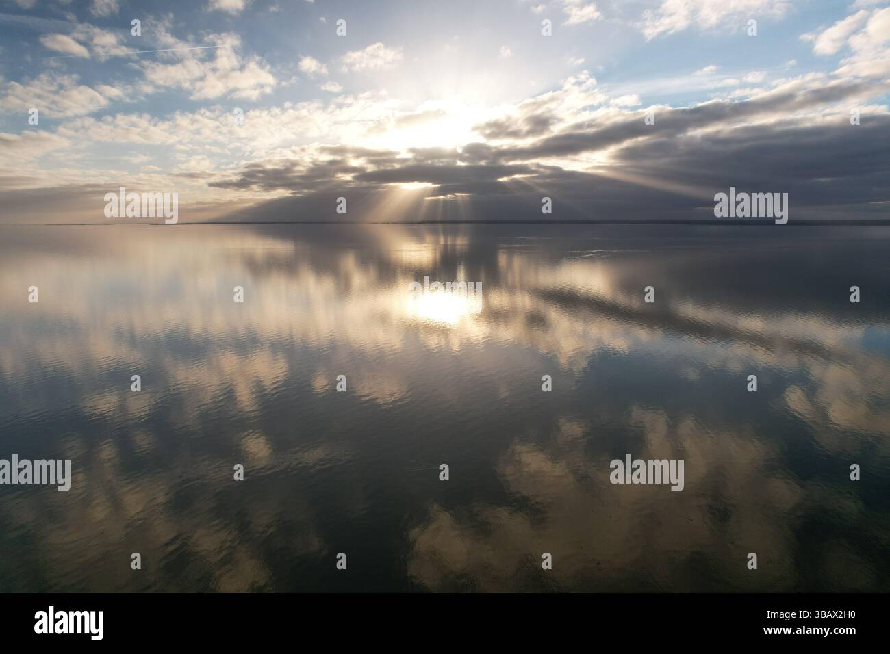 Vue aérienne, les rayons de soleil dorés traversent les nuages, se reflétant sur les eaux tranquilles du lac IJsselmeer lors d'un coucher de soleil paisible aux pays-Bas Banque D'Images