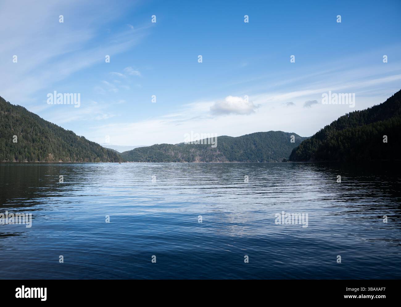 Une vue large du lac Crescent s'étend entre des crêtes boisées sous un ciel brossé de nuages doux. Banque D'Images