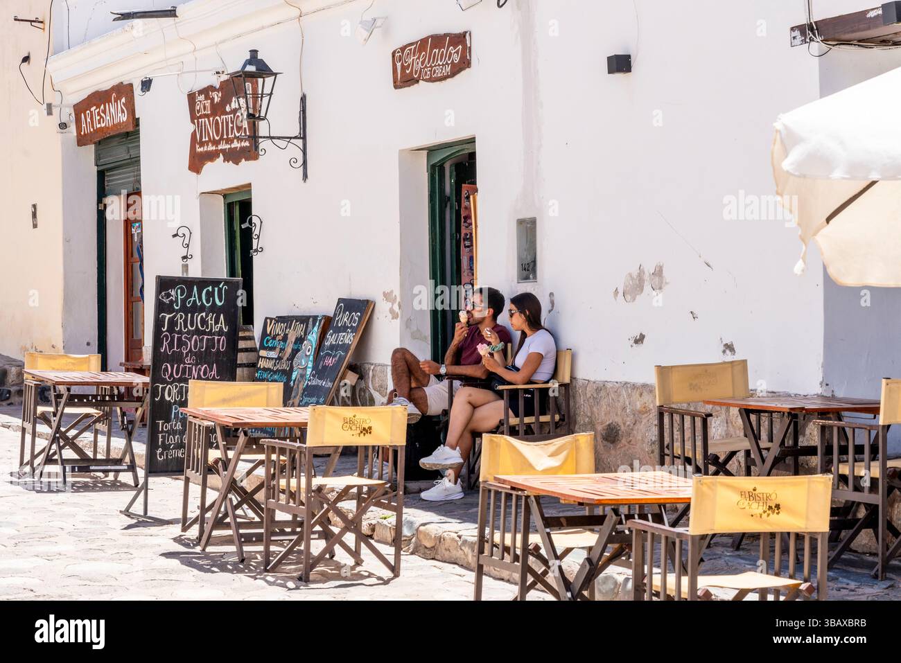 Un couple mangeant de la crème glacée devant Un café dans la ville blanchie à la chaux de Cachi, province de Salta, Argentine. Banque D'Images