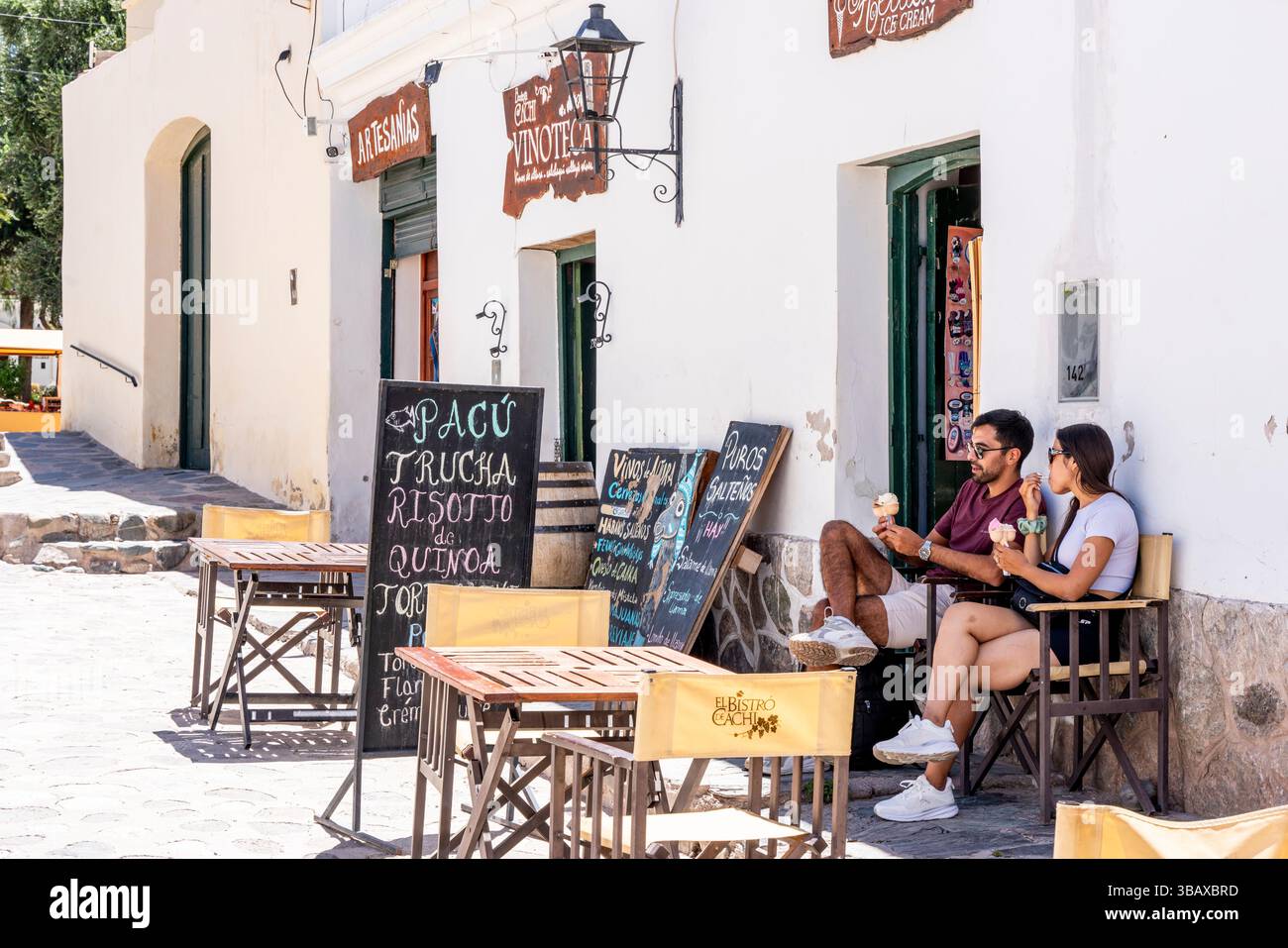 Un couple mangeant de la crème glacée devant Un café dans la ville blanchie à la chaux de Cachi, province de Salta, Argentine. Banque D'Images