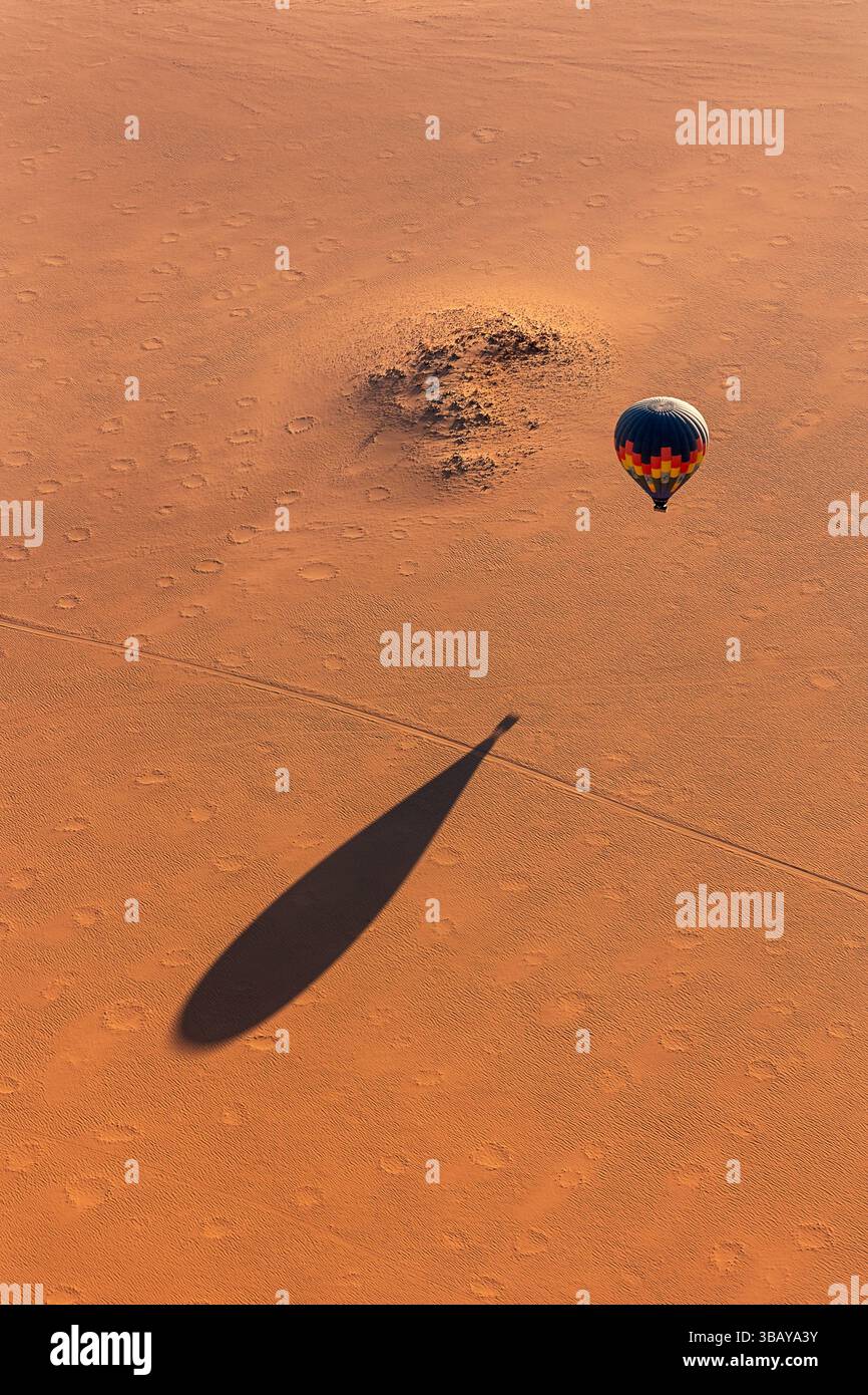 Soussvlei, Namibie - 11 juillet. 2024 : image aérienne d'un ballon chaud en vol avec son ombre sur le sable rouge et de nombreux cercles de fées sur le sol de sable. Banque D'Images