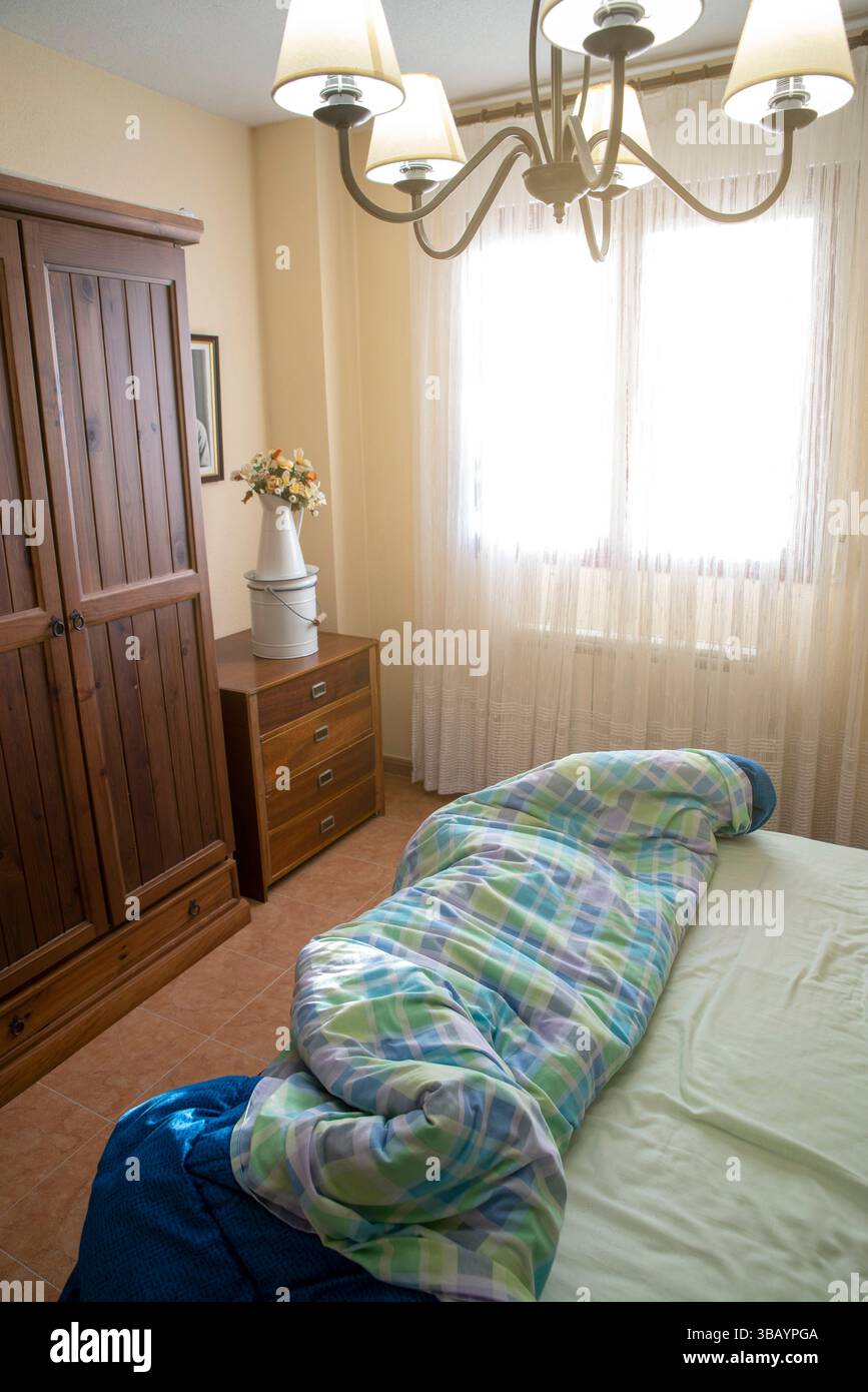 Chambre lumineuse avec lumière naturelle, mobilier en bois, atmosphère chaleureuse et couvre-lit à motifs pour une atmosphère confortable et accueillante. Banque D'Images