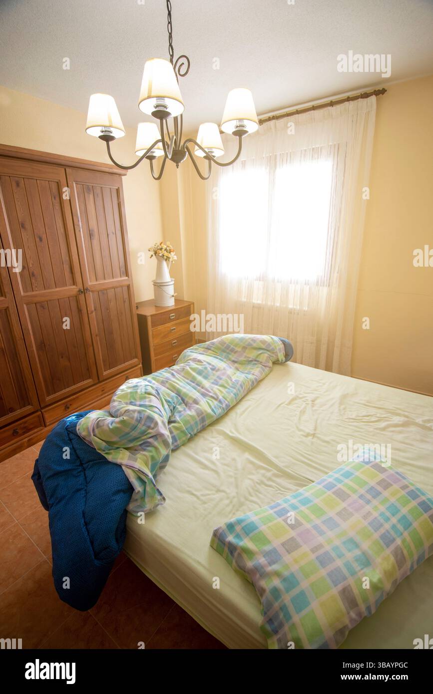 Chambre lumineuse avec lumière naturelle, mobilier en bois, atmosphère chaleureuse et couvre-lit à motifs pour une atmosphère confortable et accueillante. Banque D'Images