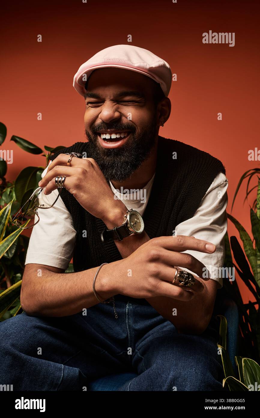 Beau jeune homme rit joyeusement tout en étant habillé dans la mode estivale entouré de plantes vibrantes Banque D'Images