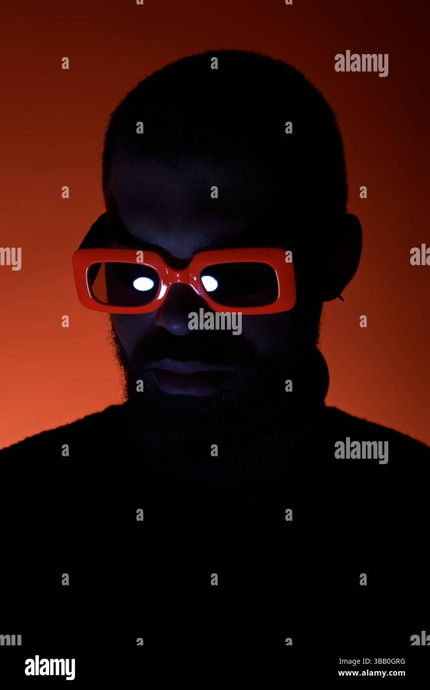 Un jeune homme arbore des lunettes orange audacieuses dans un cadre estival dynamique. Banque D'Images