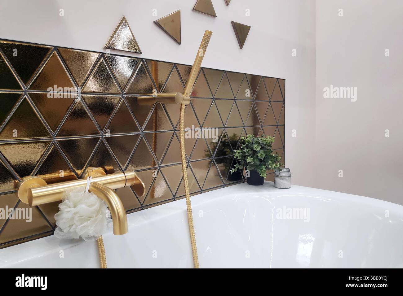 Salle de bains luxueuse et moderne, carrelage triangulaire or, luminaires en or mat, décoration minimaliste agrémentée d'une touche de verdure. Banque D'Images