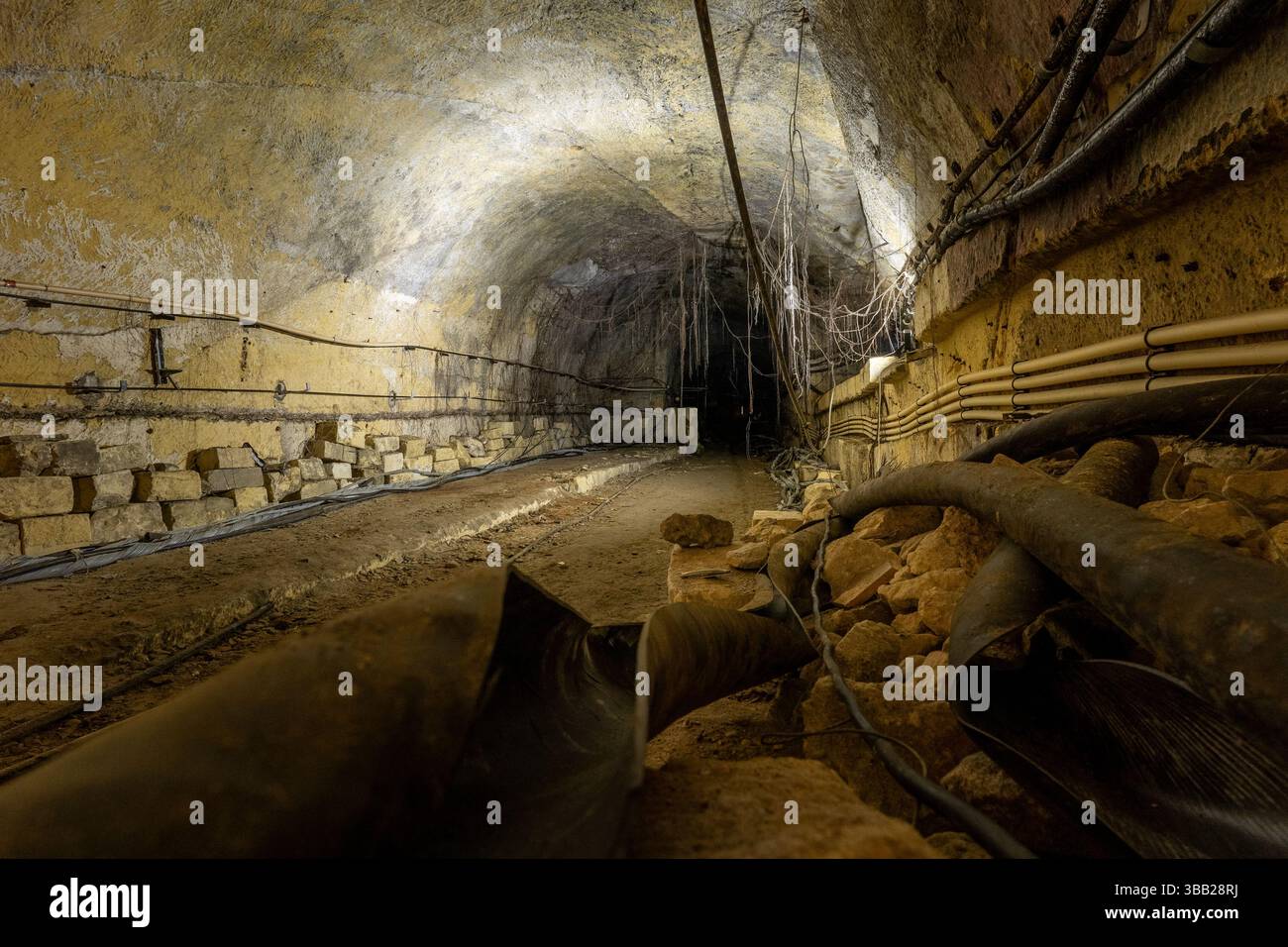 Tunnel souterrain déserté avec câbles exposés, débris et plancher rocheux Banque D'Images