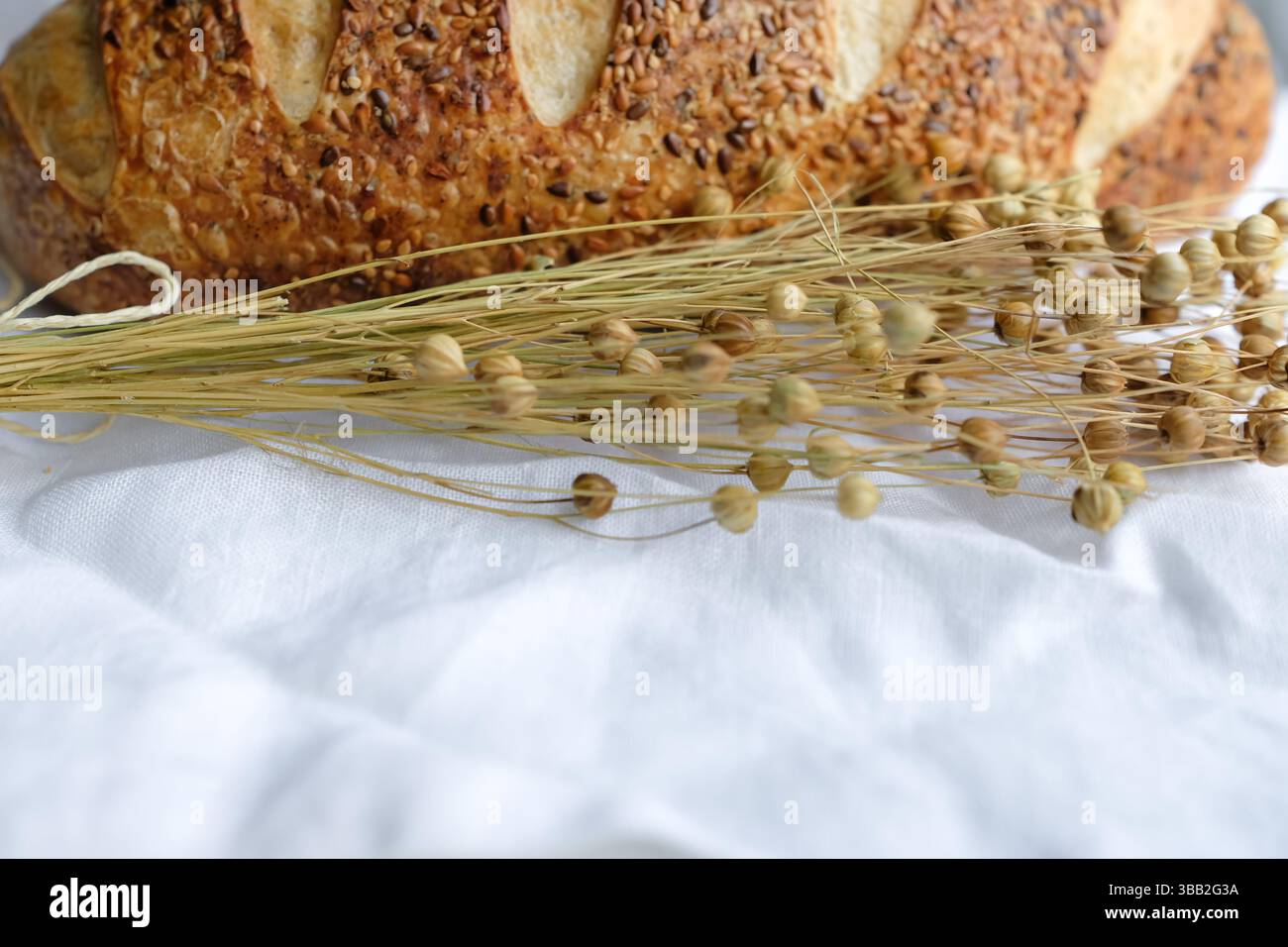 Pain saupoudré de graines de lin et de sésame sur une nappe de lin blanc. Gousses de graines de lin. Pain au levain. Banque D'Images