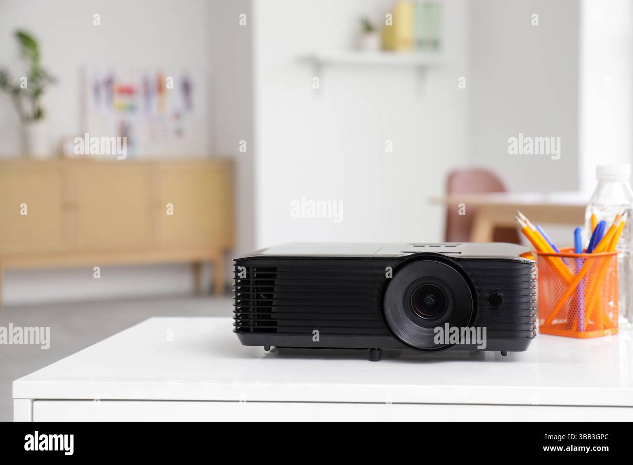 Projecteur moderne avec gobelet à crayons et bouteille d'eau sur la table du designer dans le bureau, gros plan Banque D'Images