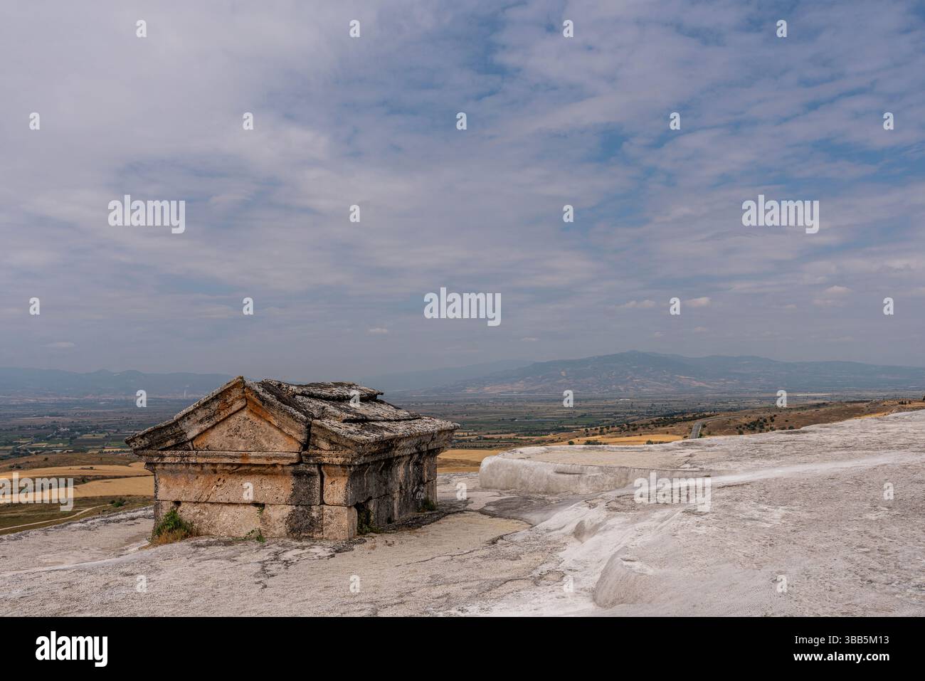 Un petit tombeau avec un toit à pignons se trouve seul dans la nécropole de Hiérapolis, entouré de travertin blanc et de montagnes lointaines. Banque D'Images