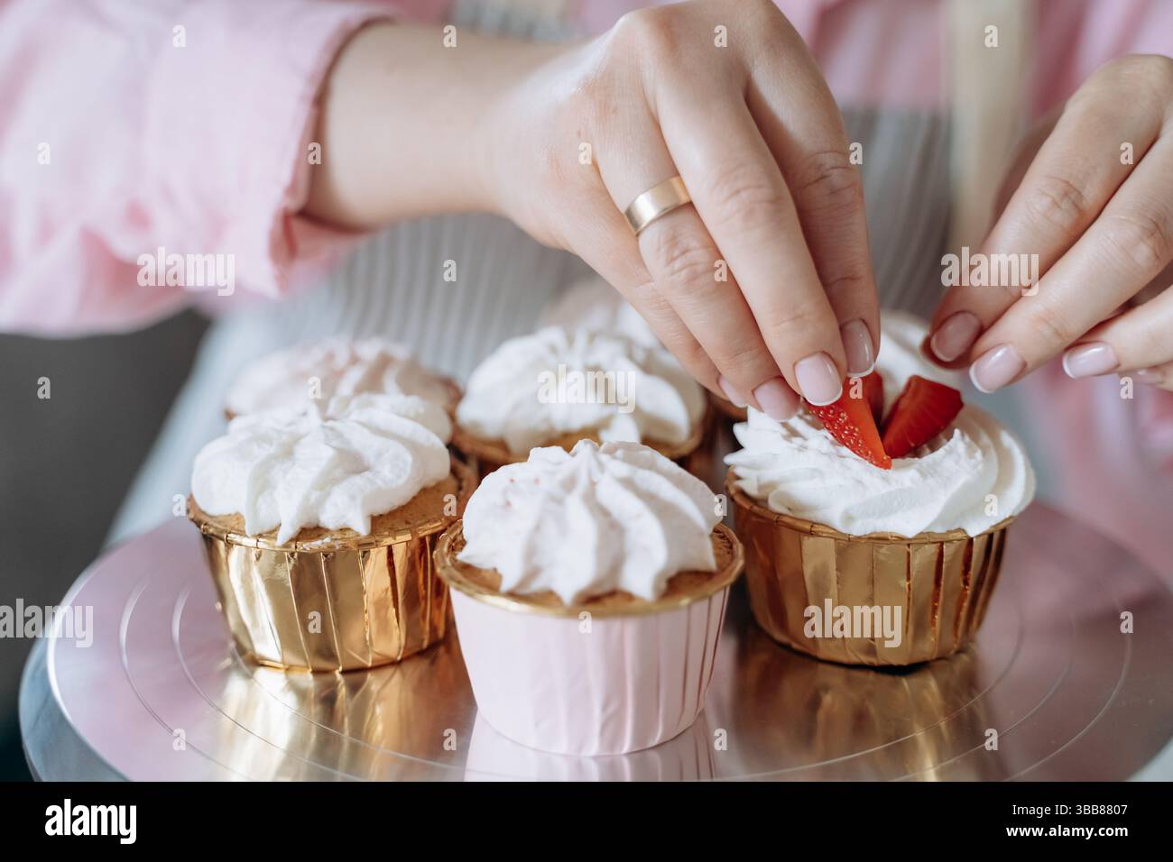 Mains disposer des tranches de fraises fraîches sur des cupcakes recouverts de crème fouettée. L'image capture le délicat processus de décoration des desserts pour un vi Banque D'Images