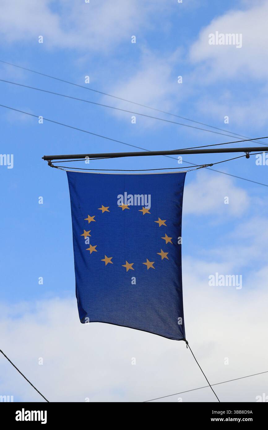 Drapeau de l'Union européenne avec des étoiles jaunes suspendues au mât du drapeau contre l'orientation verticale du ciel nuageux Banque D'Images