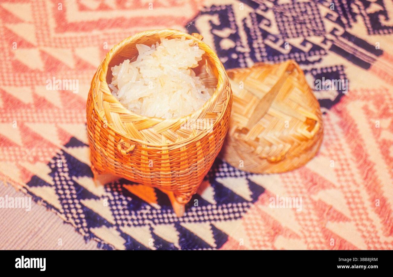 Un récipient traditionnel thaïlandais à riz collant, appelé Kratip, est ouvert, révélant le riz fraîchement cuit à l'intérieur. Le Kratip est fait de bambou tissé et Banque D'Images