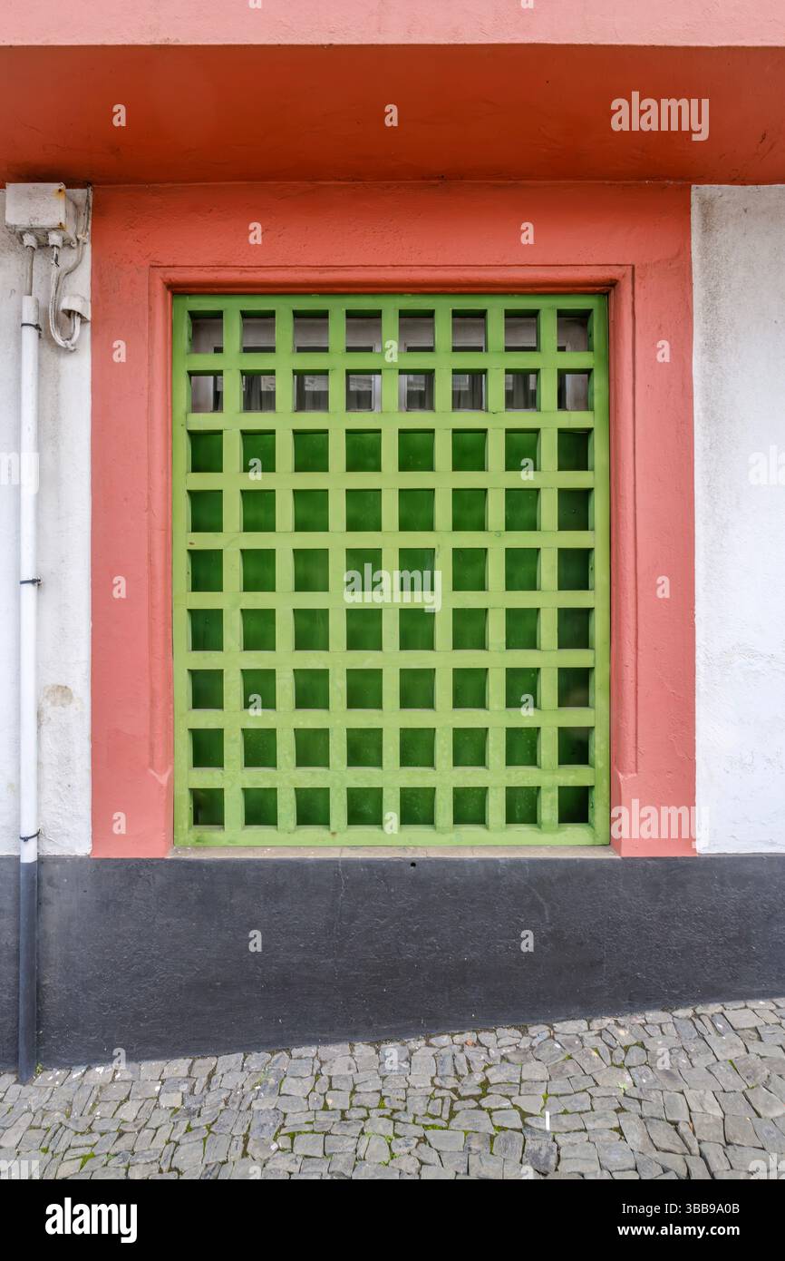 Fenêtre en treillis vert vibrant avec cadre coloré, Terceira. Gros plan attrayant d'une fenêtre de style treillis vert vif dans un cadre rouge et pêche Banque D'Images