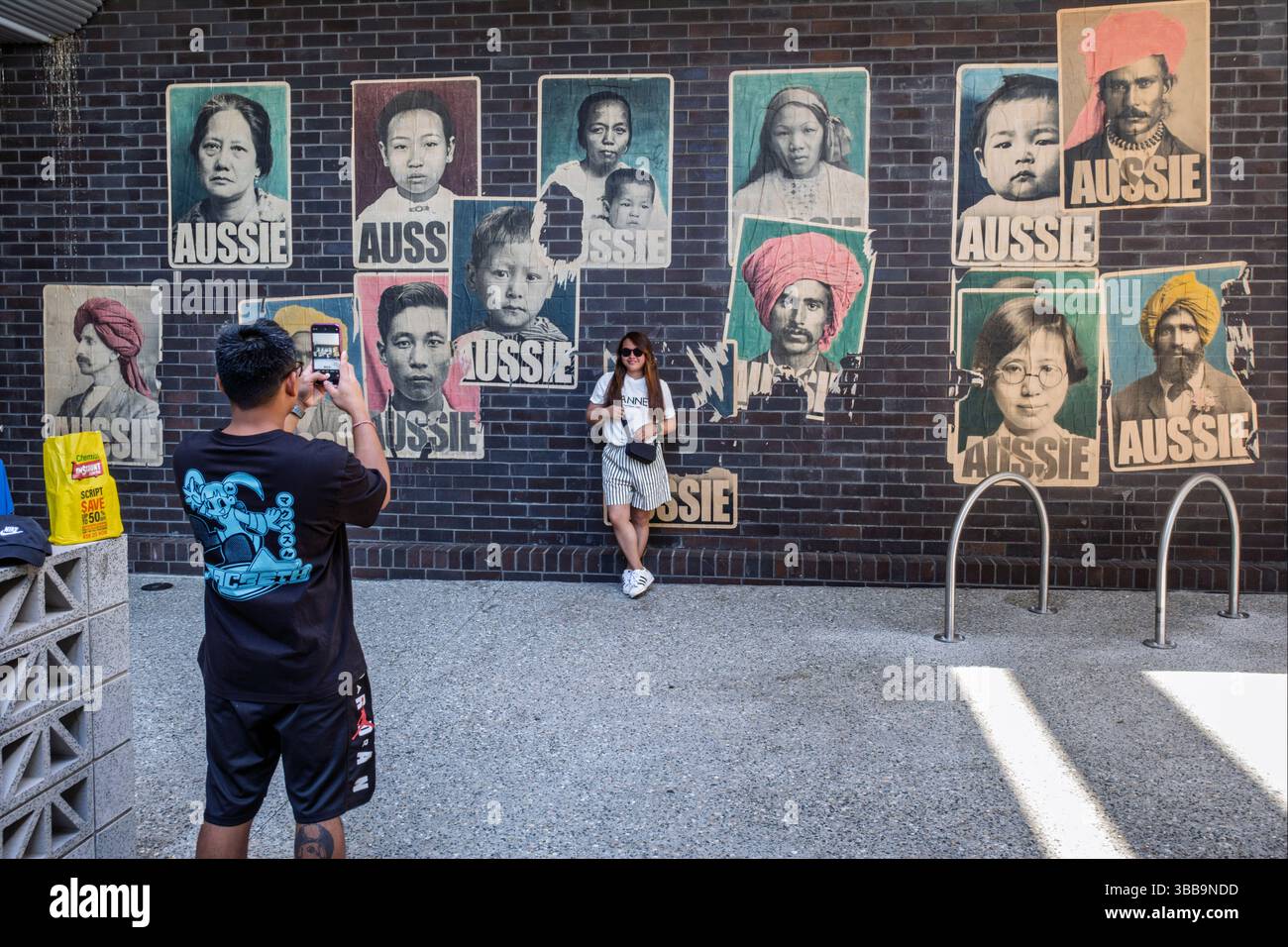 À Fremantle, en Australie occidentale, un touriste pose devant les emblématiques affiches « australiennes » de Peter Drew représentant des immigrants du début du XXe siècle en Australie Banque D'Images