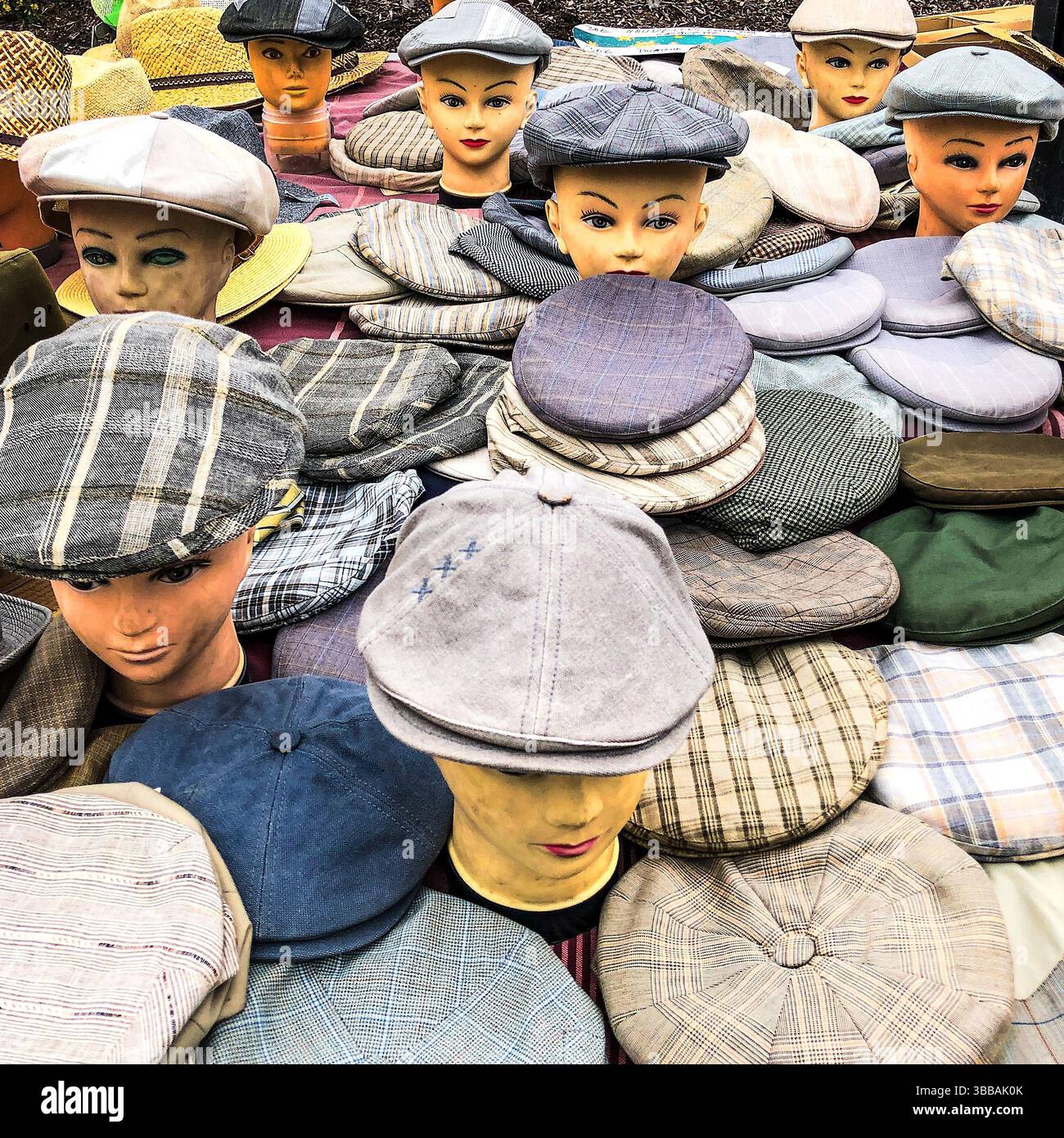 Stand de marché avec des têtes de mannequin portant un assortiment de casquettes plates - France. Banque D'Images