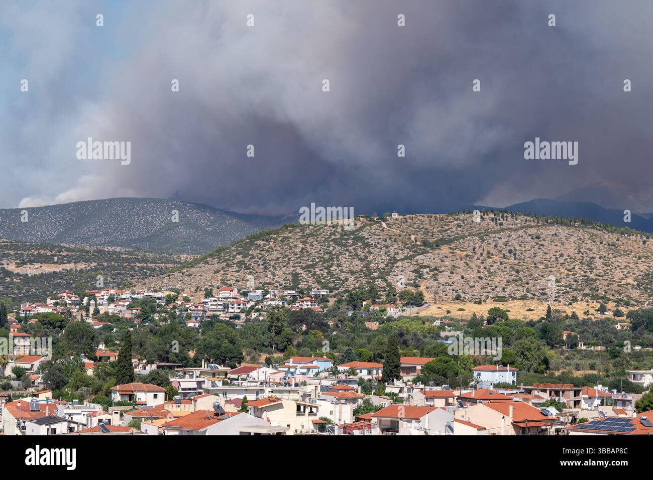 La fumée épaisse d'un feu de forêt s'élève derrière une zone résidentielle, montrant la proximité des catastrophes naturelles avec les environnements urbains dans un climat de réchauffement Banque D'Images