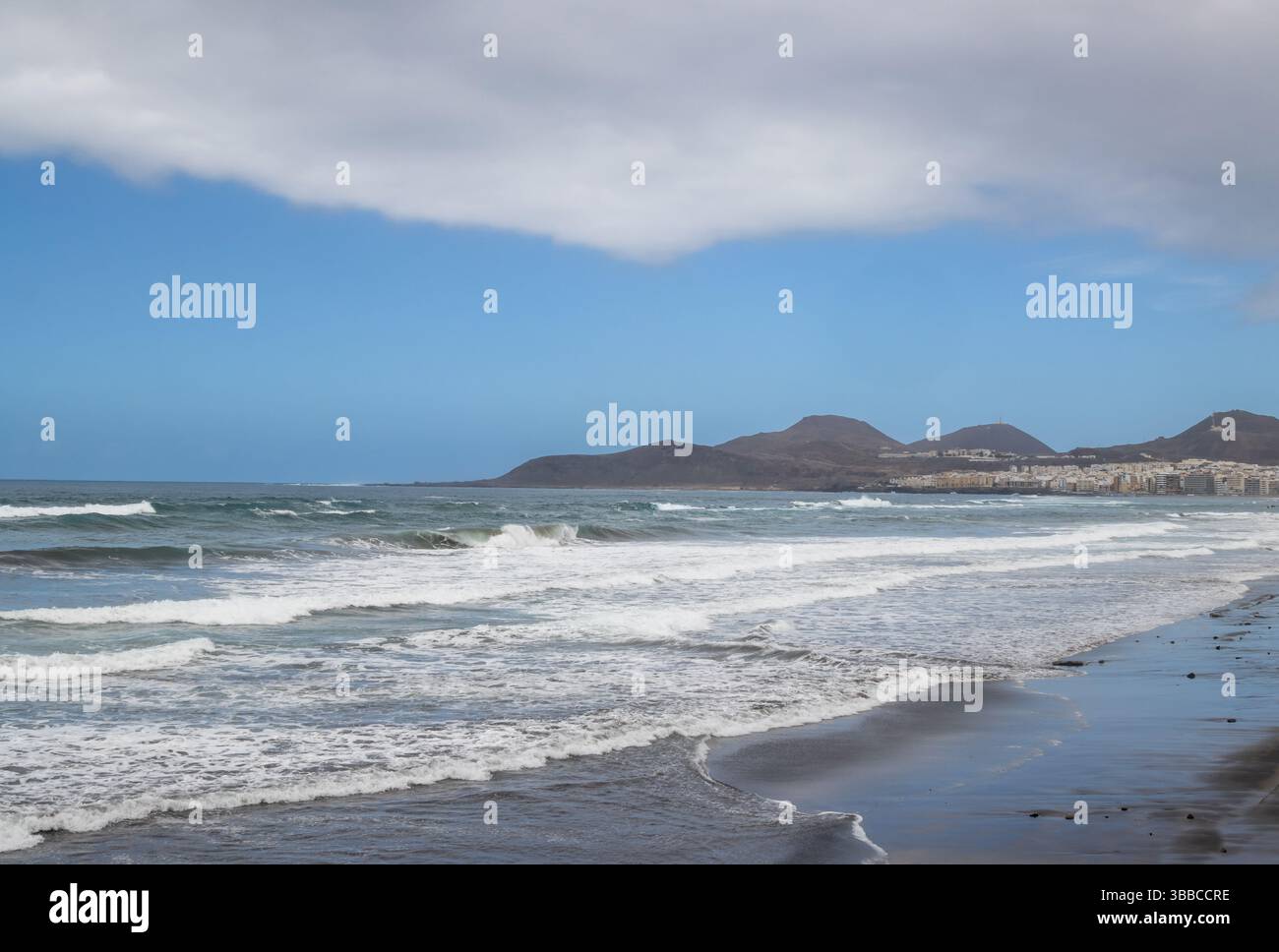 Plage de sable avec vagues de l'océan Atlantique. Montagnes à l'horizon. Ciel bleu avec des nuages blancs. Las Palmas de Gran Canaria, Îles Canaries, Espagne. Banque D'Images