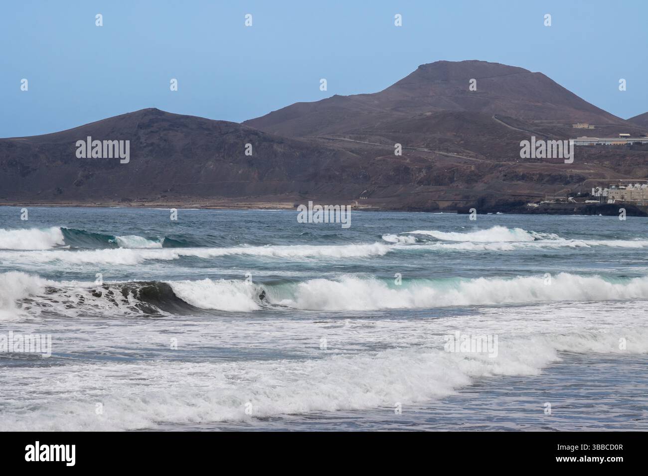 Plage de sable avec vagues de l'océan Atlantique. Montagnes à l'horizon. Ciel bleu avec des nuages blancs. Las Palmas de Gran Canaria, Îles Canaries, Espagne. Banque D'Images