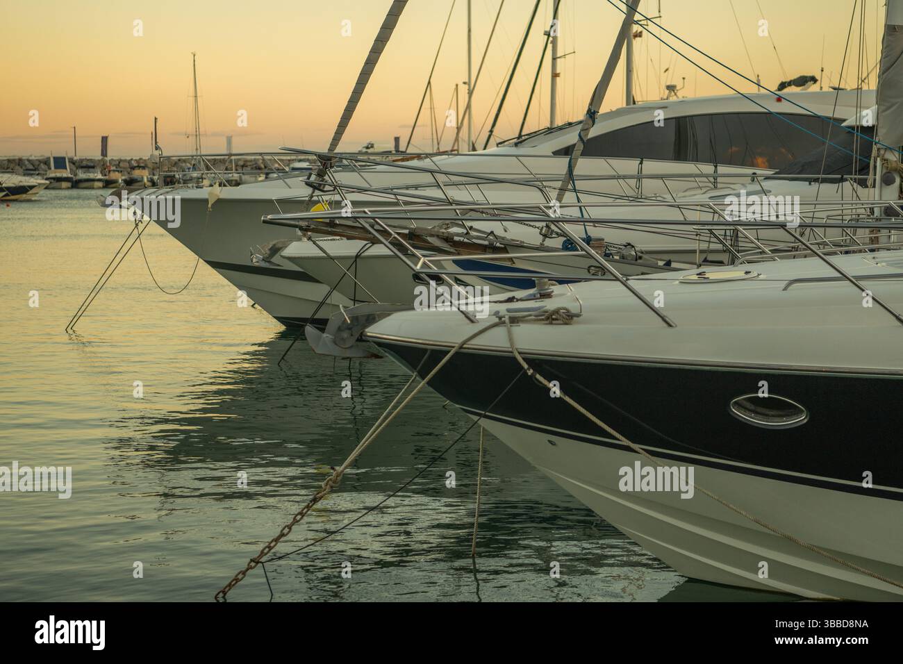 Une soirée paisible à la marina propose plusieurs bateaux qui se mettent doucement dans l'eau alors que le soleil se couche à l'horizon. Le ciel passe à des teintes douces o Banque D'Images