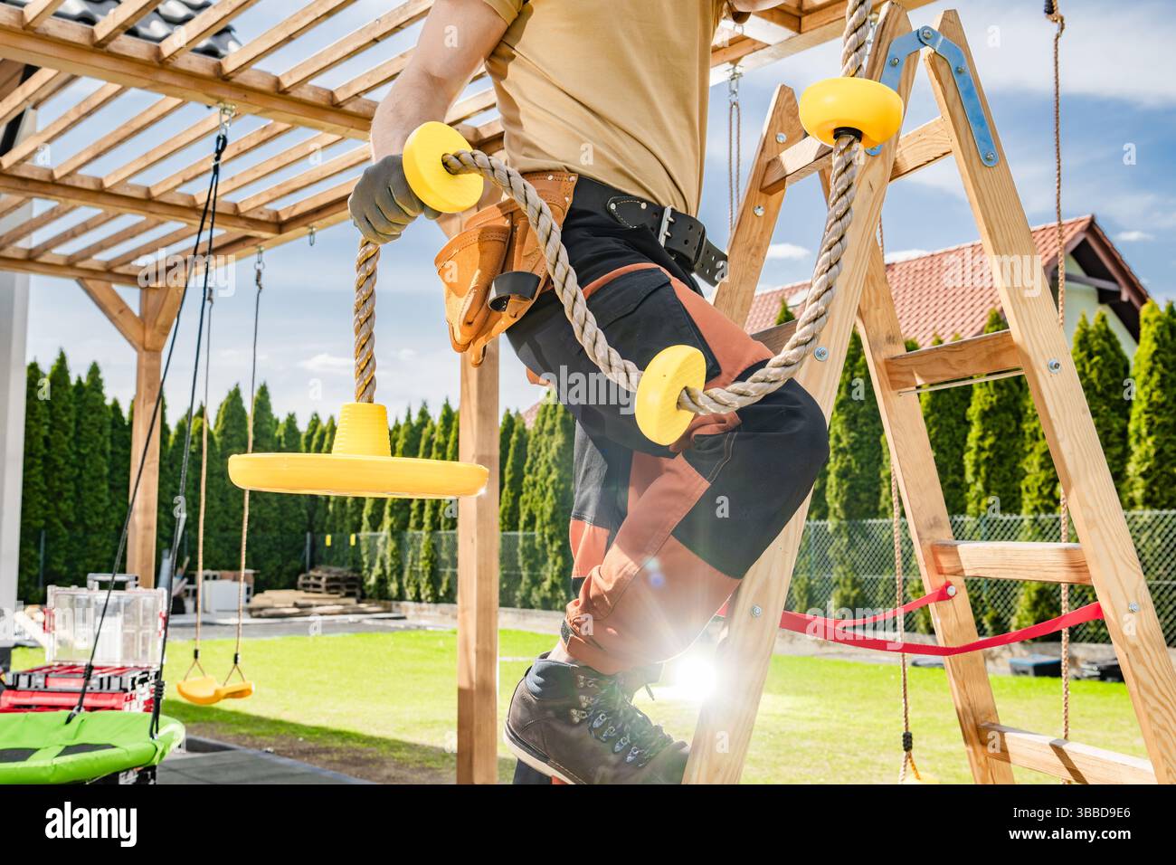 Un travailleur de la construction est engagé dans l'installation de nouveaux équipements de terrain de jeu dans une aire de loisirs extérieure. Portant des gants et des bottes robustes, le Banque D'Images