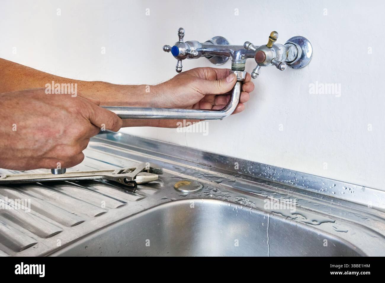 Pendant la réparation du robinet, le plombier monte le bec courbé sur le robinet à double poignée au-dessus de l'évier en acier inoxydable, les raccords d'eau sont encastrés dans le mur en béton, wrenc Banque D'Images