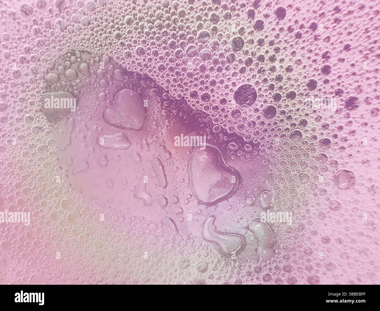 Empreinte de coeur dans des bulles de mousse savonneuse laisse une traînée d'empreintes dans un motif abstrait montrant l'amour et le soin sur la surface rose humide de couleur pastel violet. Banque D'Images