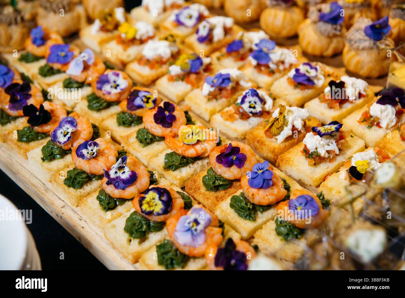 Petits canapés élégants garnis de crevettes, pesto, mélange bruschetta et fleurs comestibles, servis sur du pain grillé pour les événements de restauration. Banque D'Images