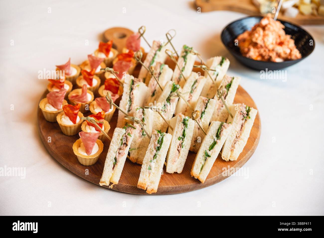 Assortiment de sandwiches et canapés savoureux avec jambon et crème, magnifiquement disposés sur un plateau en bois pour un événement. Banque D'Images