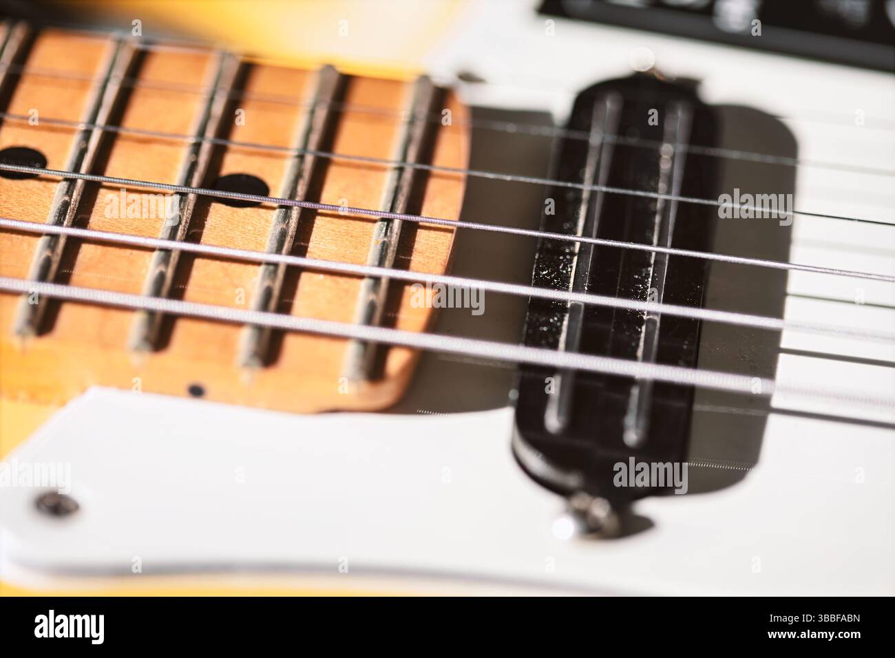 Vue d'une touche de guitare électrique jaune, présentant des frettes et des cordes en métal avec un garde-piquet noir en dessous. La faible profondeur de champ met en évidence la texture Banque D'Images