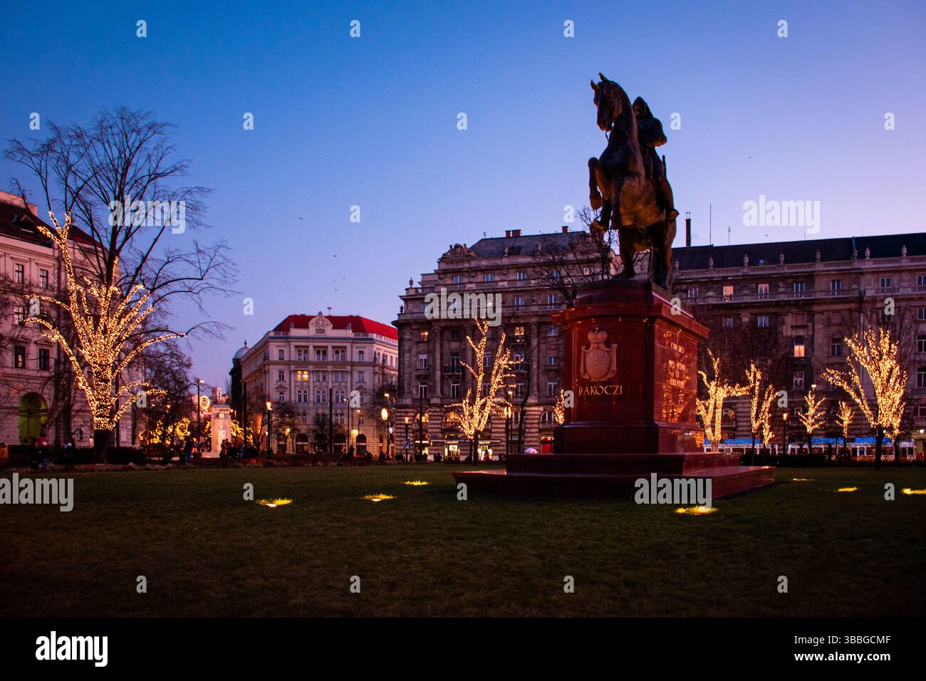 Place de Budapest au crépuscule : lumières douces, un ciel qui s'estompe dans le bleu, et une atmosphère enchanteresse embrassant l'architecture historique. Banque D'Images