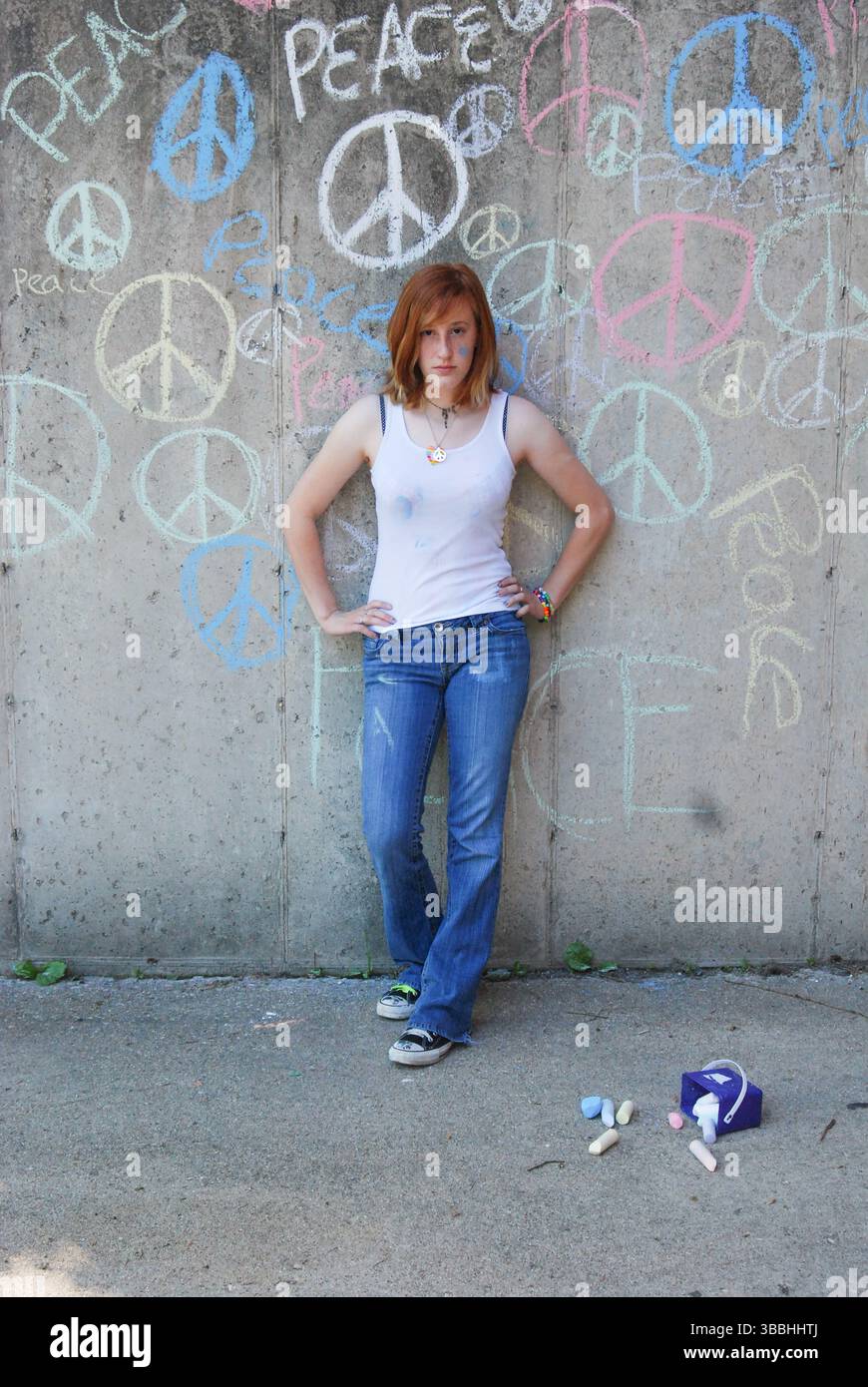 Jeune femme devant le mur de ciment avec des signes de paix à la craie graffiti Banque D'Images