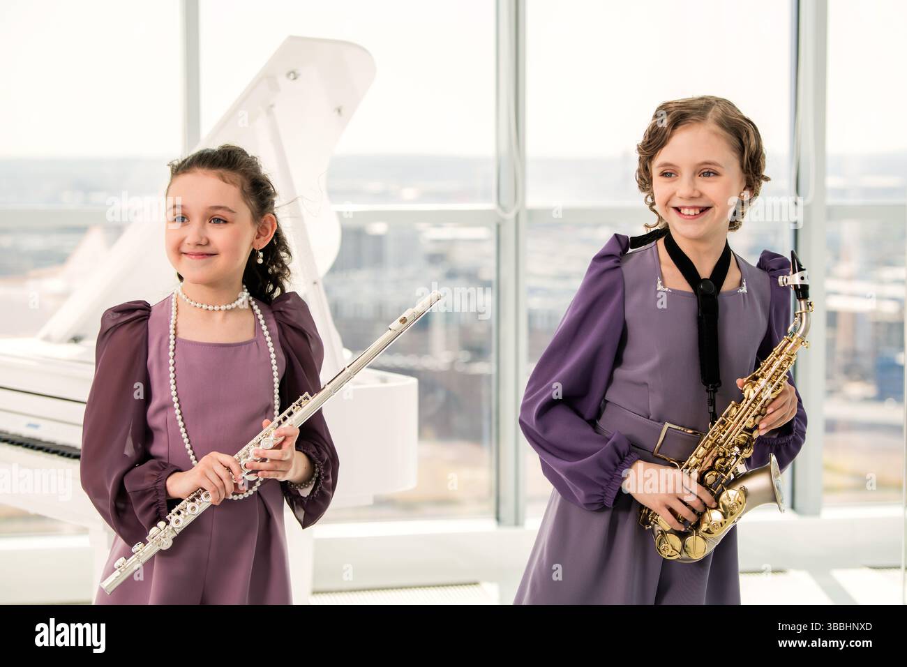 Deux filles jouent de la flûte et du saxophone dans une pièce lumineuse avec piano Banque D'Images