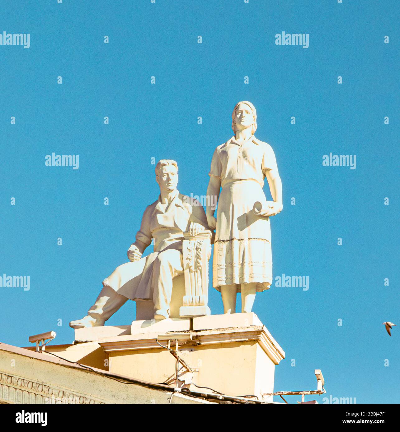 Sculpture monumentale d'un homme et d'une femme tenant des outils, capturés contre un ciel bleu clair. Banque D'Images