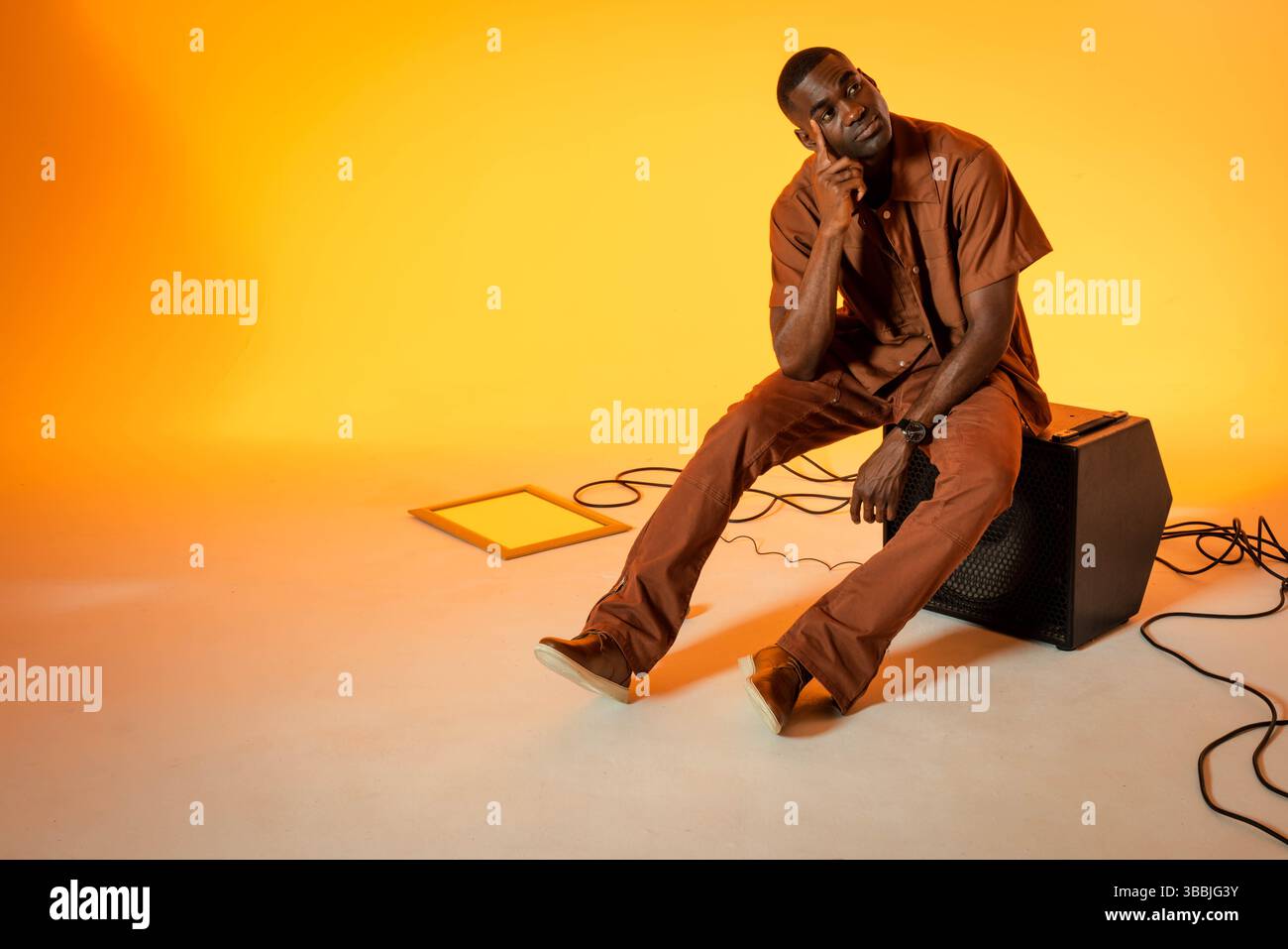 Assis homme afro-américain regardant vers le haut dans le studio, avec ampli, câbles, panneau d'éclairage, espace de copie Banque D'Images