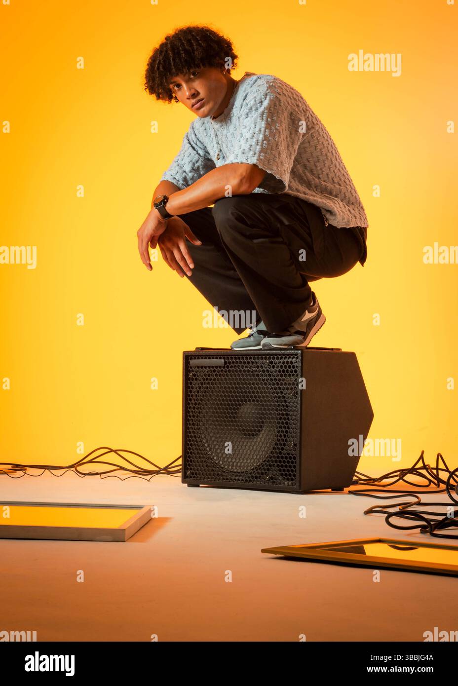 Homme afro-américain accroupi équilibrant au sommet de l'amplificateur en studio, avec des câbles audio Banque D'Images