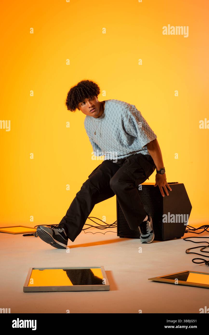 Modèle masculin adulte assis portant un pull texturé sur la boîte de haut-parleur dans le studio, avec des miroirs et des câbles Banque D'Images