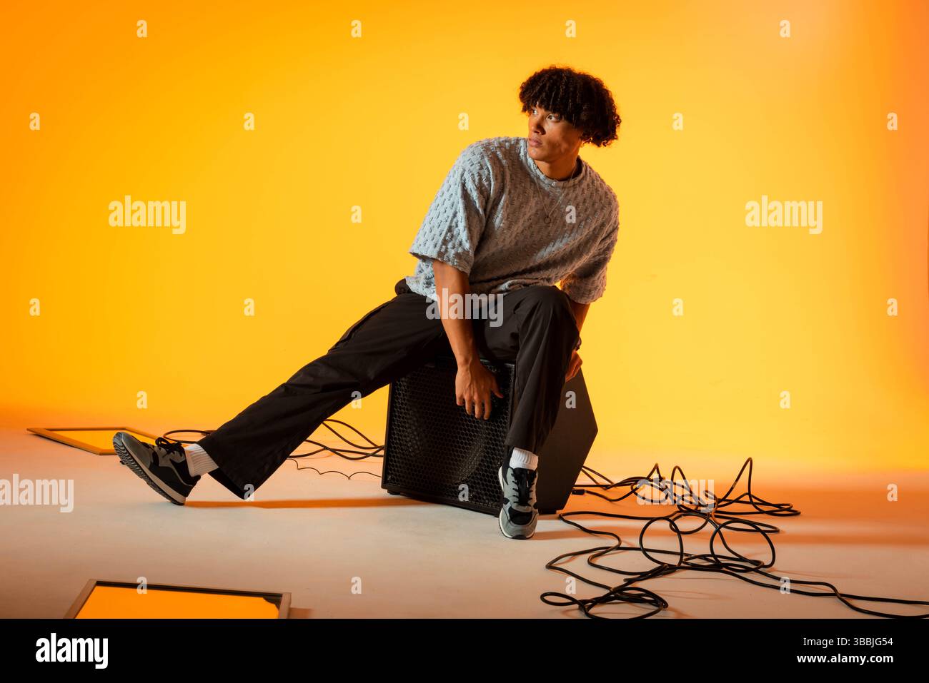 Assis homme afro-américain portant T-shirt sur haut-parleur noir en studio, avec des lumières LED, des câbles Banque D'Images