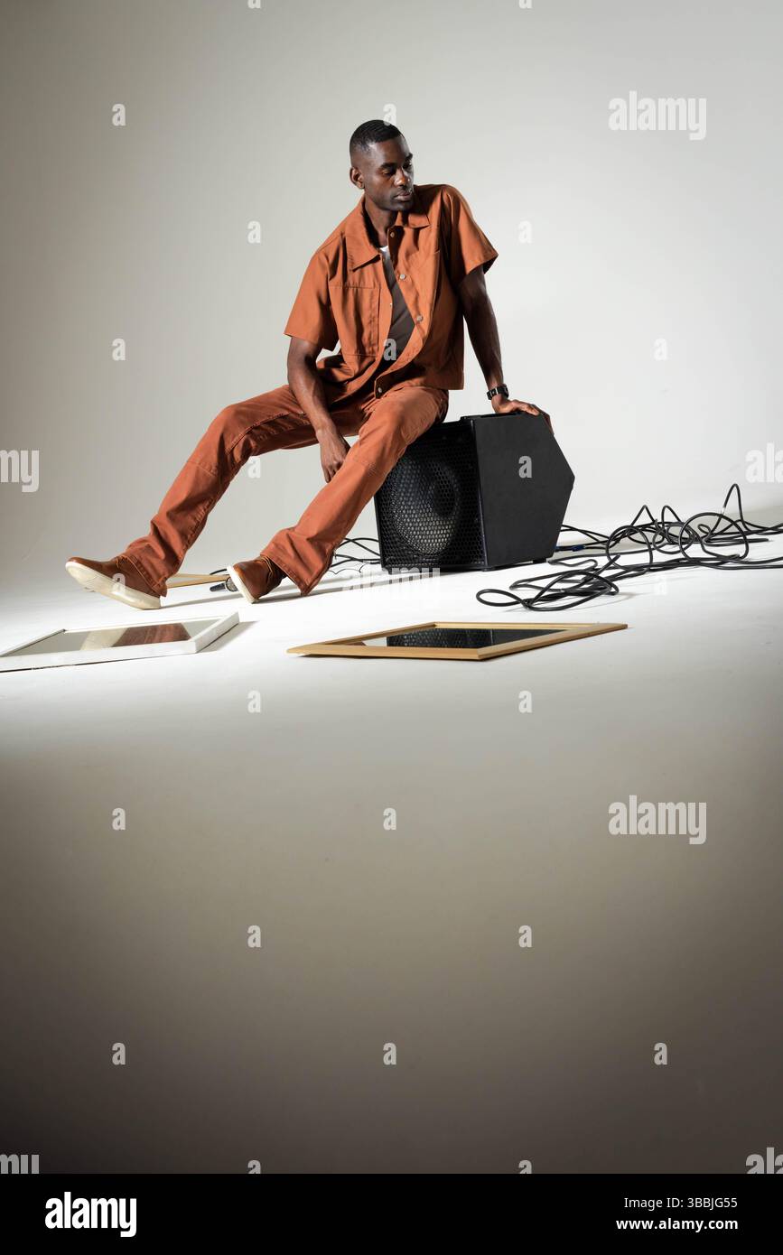 Homme afro-américain penché portant une chemise rouille sur le caisson de basses de haut-parleur en studio, avec des câbles enroulés Banque D'Images
