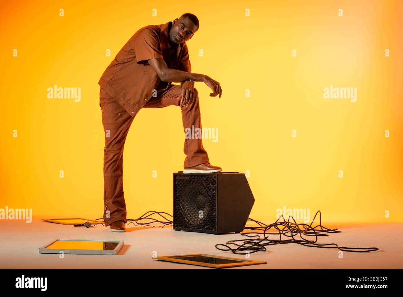 Posant homme afro-américain sur le cabinet de haut-parleur en studio, avec micro, câbles et écrans, espace de copie Banque D'Images