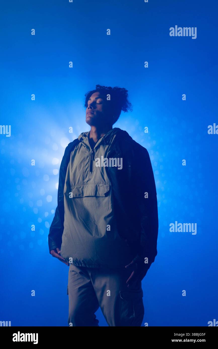 Homme debout face vers le haut avec les yeux fermés dans le studio de photographie, soulignant les faisceaux de lumière bleue Banque D'Images