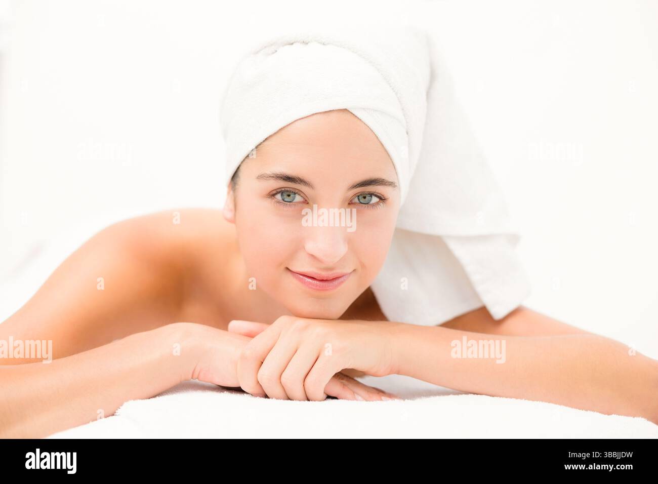 Femme relaxante reposant sur une table de spa dans la salle de bien-être, avec serviette turban et drap blanc Banque D'Images
