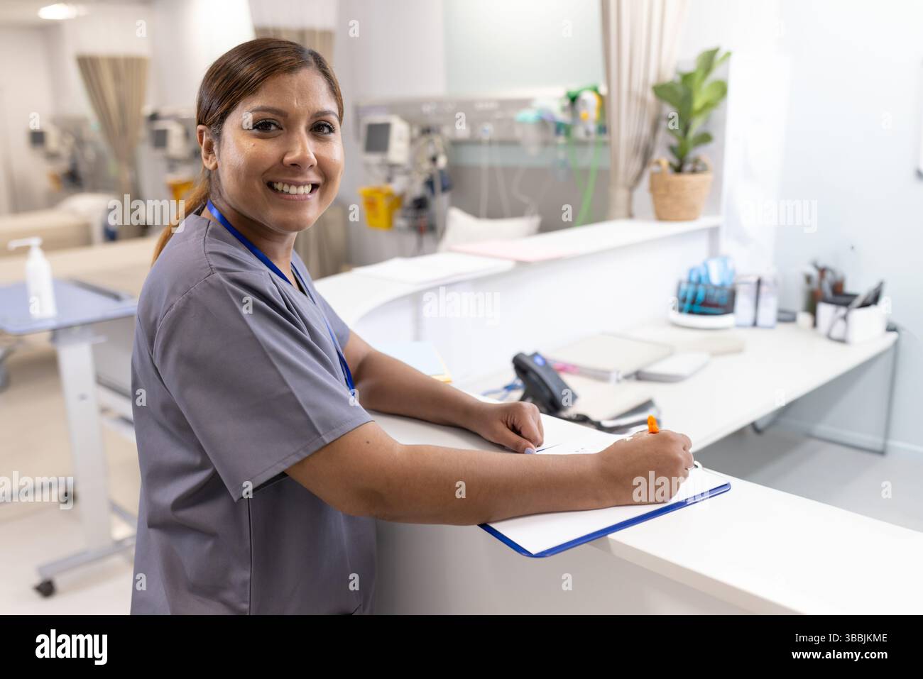 Infirmière adulte mature écrivant sur un bloc-notes avec un stylo orange au bureau du service hospitalier, avec des pompes à perfusion Banque D'Images