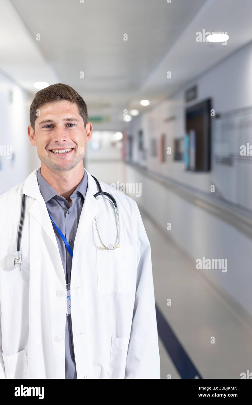 Médecin masculin debout et souriant dans le couloir de l'hôpital, avec stéthoscope et badge d'identification, espace de copie Banque D'Images