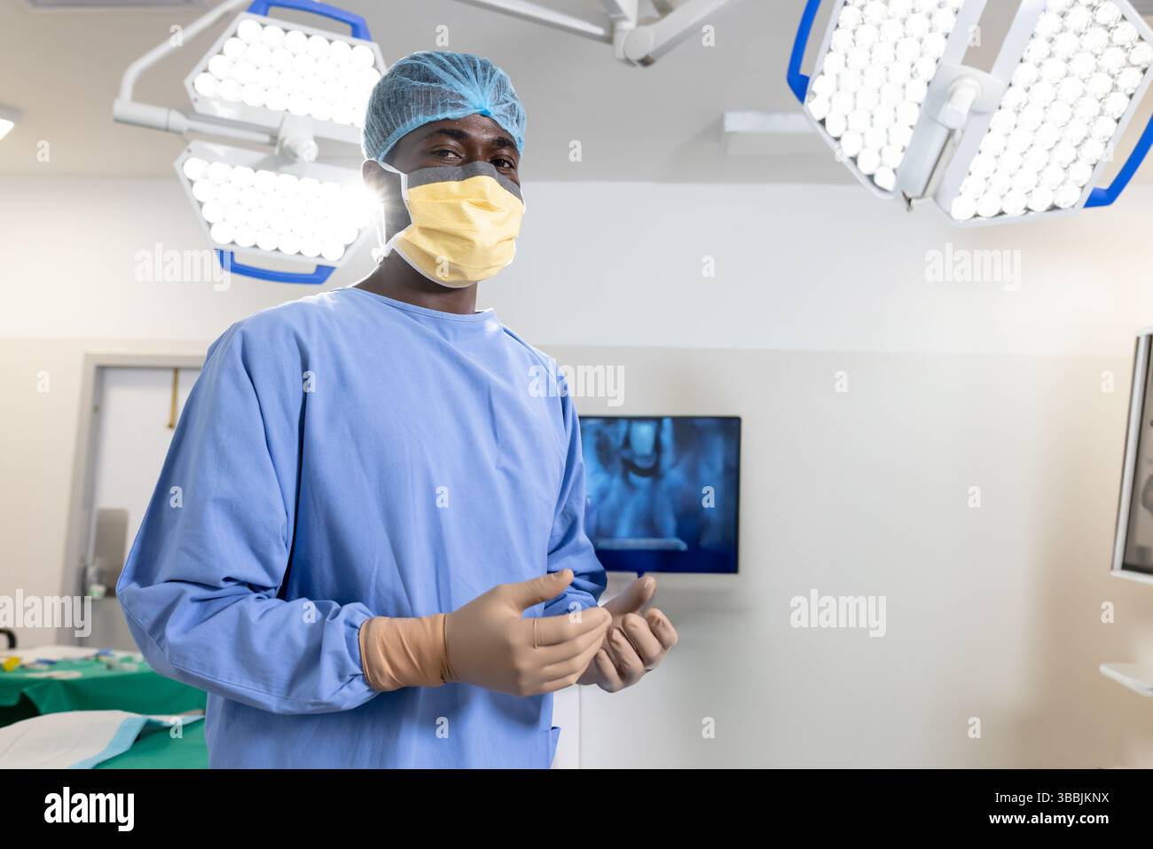 Chirurgien afro-américain portant gants et masque au bloc opératoire avec lumières chirurgicales Banque D'Images
