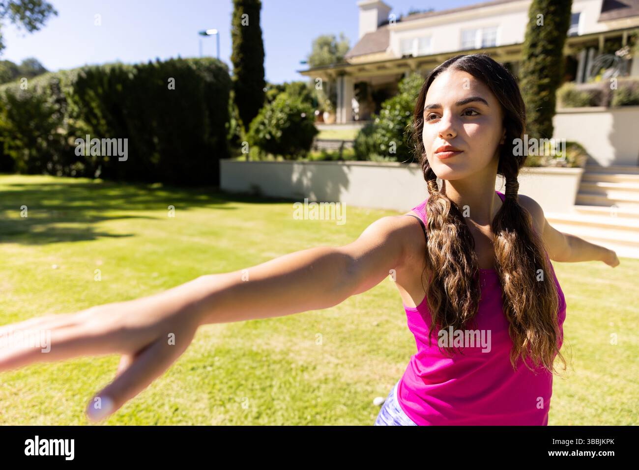Jeune femme effectuant un étirement de yoga sur une pelouse bien entretenue devant la maison de banlieue, espace de copie Banque D'Images
