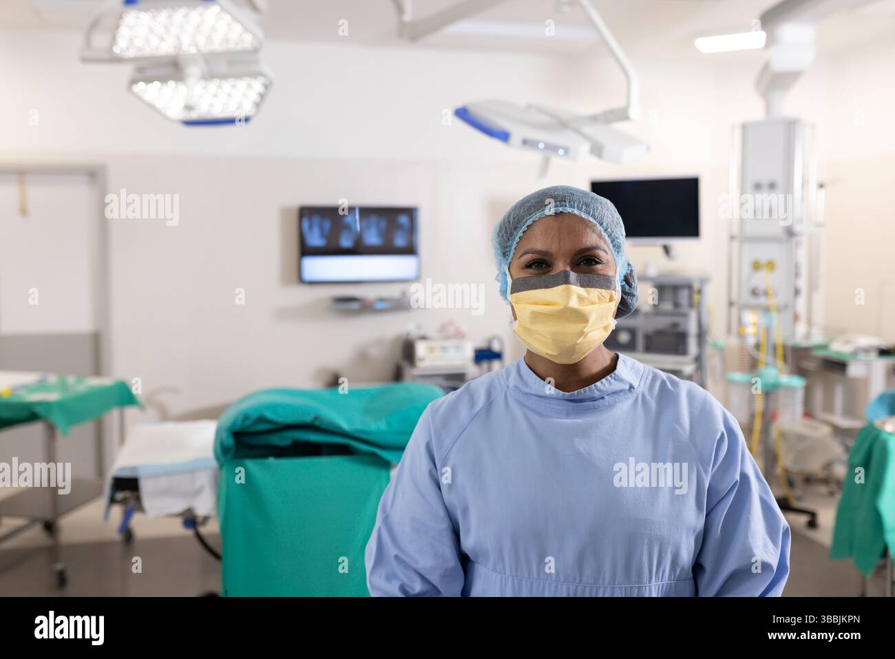 Infirmière multiraciale debout en salle d'opération, avec des lampes et du matériel chirurgicaux suspendus Banque D'Images